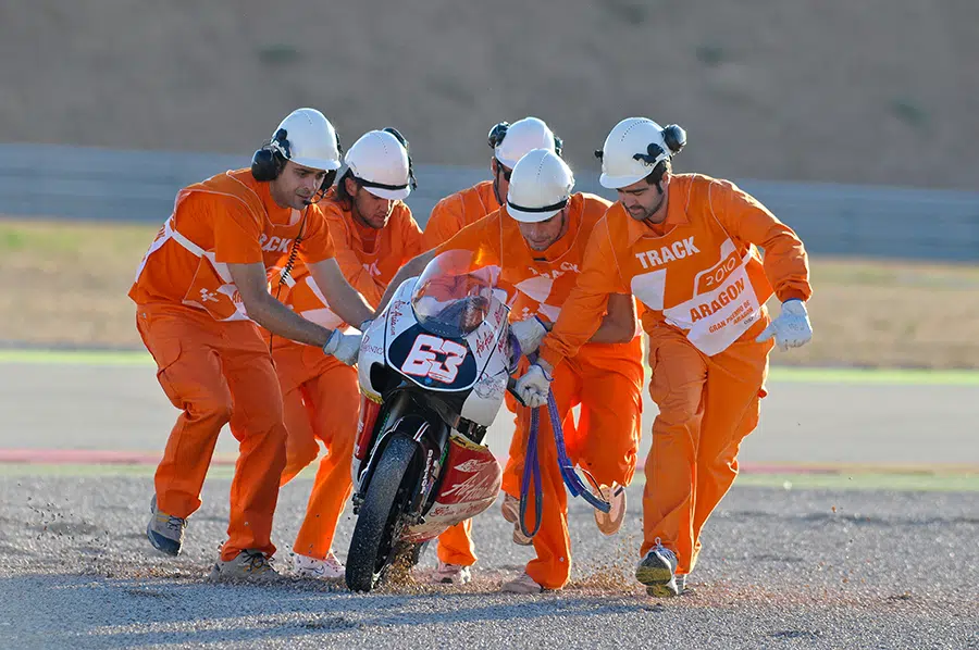 Comisarios de pista recogiendo una motocicleta tras una caída, garantizando la seguridad en la carrera