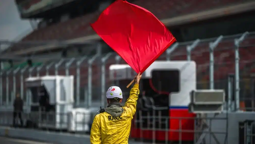 Comisario de pista sosteniendo la bandera roja, señalizando una interrupción en la carrera